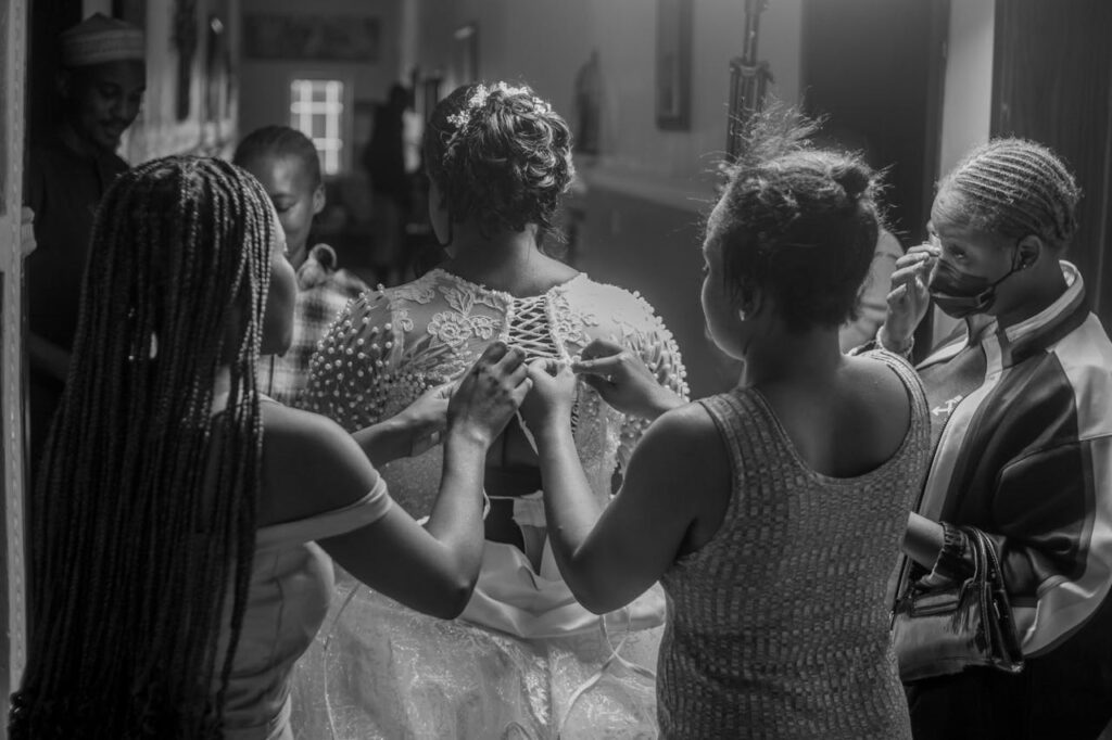 Black and white photo capturing bridal preparation with bridesmaids assisting.